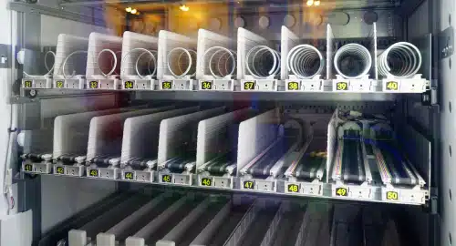 A close-up of an automated filing or storage system with labeled slots numbered 31 to 50, each holding white, curved sheets or trays, inside a glass-enclosed cabinet with visible wiring and metal components.